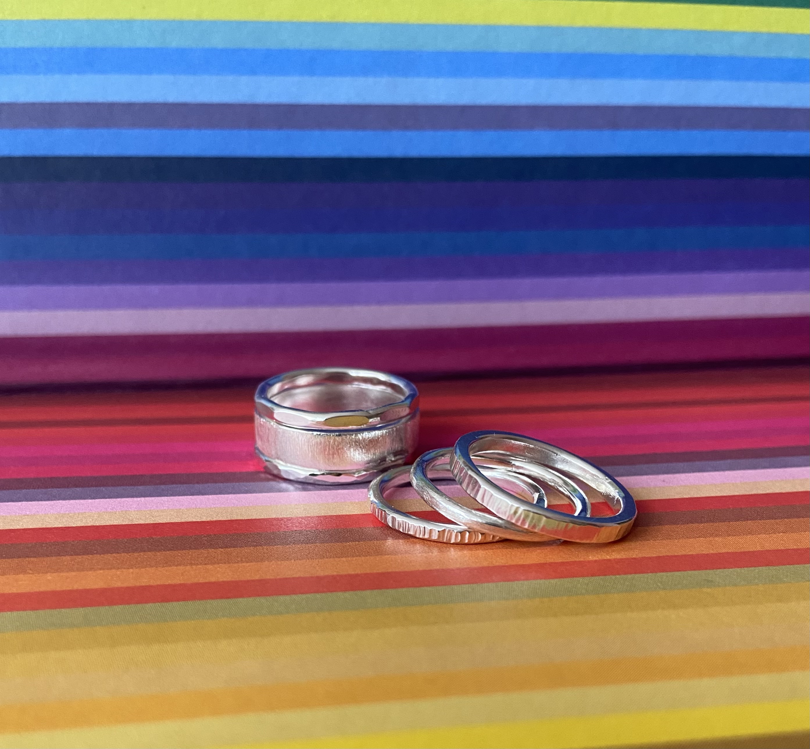 Handcrafted silver stacking rings with different textures on a colourful striped background